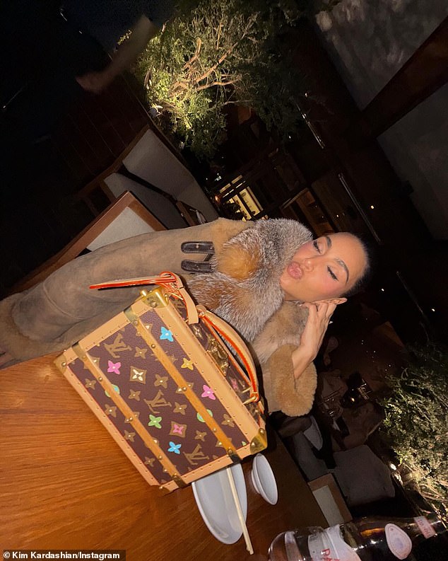 Kim enrugou os lábios na mesa com sua cara saco de caixa da Louis Vuitton, que apoiava com destaque em primeiro plano