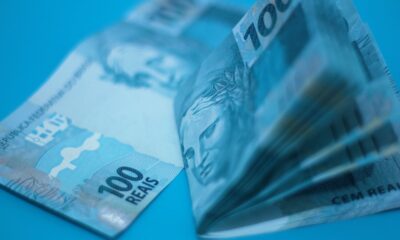 Pilha de cédulas de 100 reais sobre superfície azul, ilustrando a inflação medida pelo IPCA-15