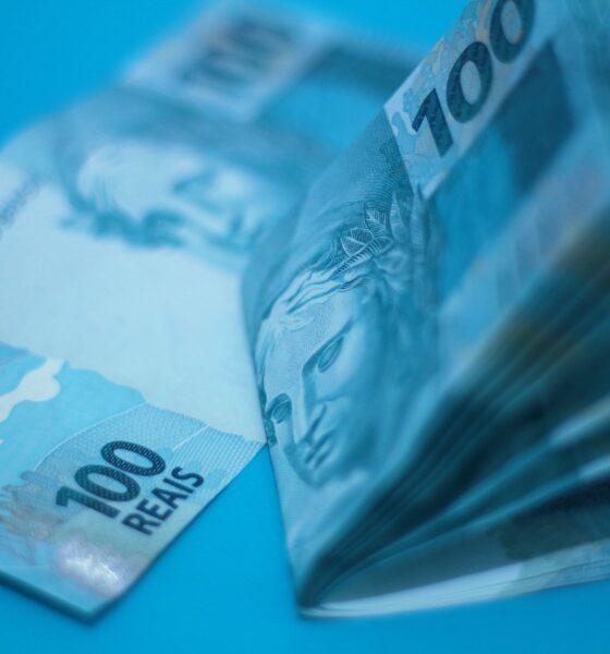 Pilha de cédulas de 100 reais sobre superfície azul, ilustrando a inflação medida pelo IPCA-15
