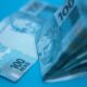 Pilha de cédulas de 100 reais sobre superfície azul, ilustrando a inflação medida pelo IPCA-15